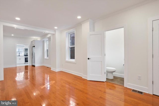 empty room with visible vents, baseboards, light wood-style flooring, and crown molding