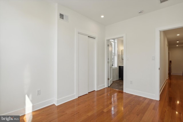 unfurnished bedroom with hardwood / wood-style flooring, a closet, and ensuite bath