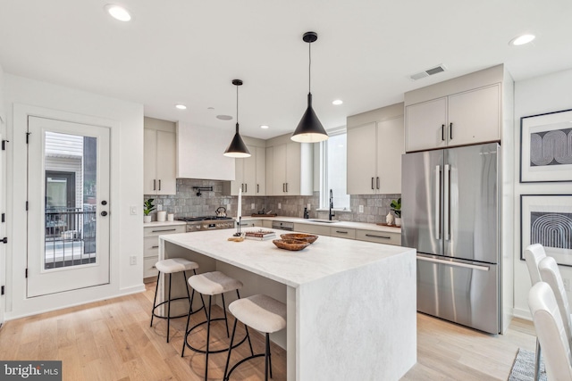 kitchen featuring a kitchen island with sink, sink, light hardwood / wood-style floors, hanging light fixtures, and appliances with stainless steel finishes