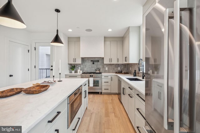 kitchen with light stone counters, light hardwood / wood-style floors, custom exhaust hood, appliances with stainless steel finishes, and decorative light fixtures