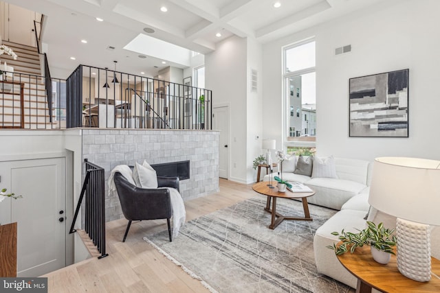 living room with light wood-type flooring, coffered ceiling, a towering ceiling, a skylight, and beam ceiling