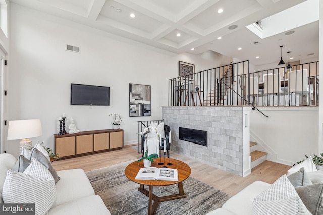 living room featuring beam ceiling, coffered ceiling, a high ceiling, and light hardwood / wood-style flooring