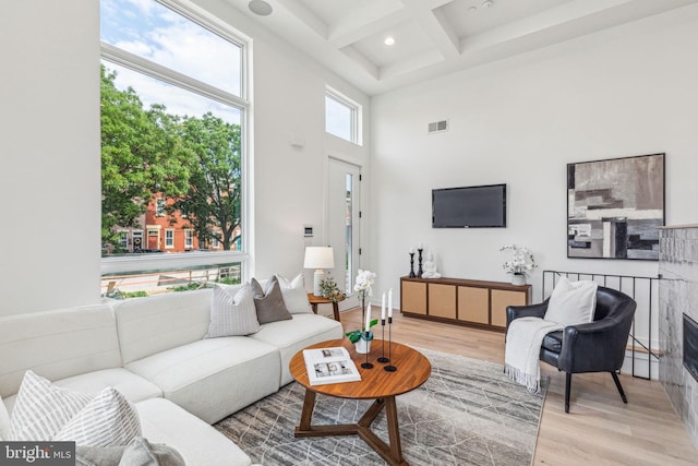 living room featuring beam ceiling, coffered ceiling, a high ceiling, and light hardwood / wood-style floors