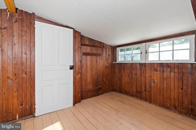 unfurnished room with wood walls, lofted ceiling, and light wood-type flooring