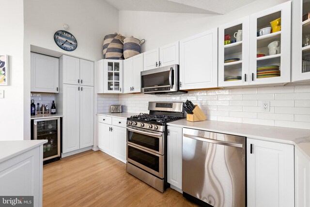 kitchen with lofted ceiling, white cabinetry, beverage cooler, and stainless steel appliances