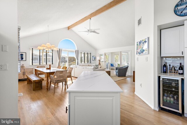 kitchen with beam ceiling, beverage cooler, white cabinetry, and light hardwood / wood-style flooring