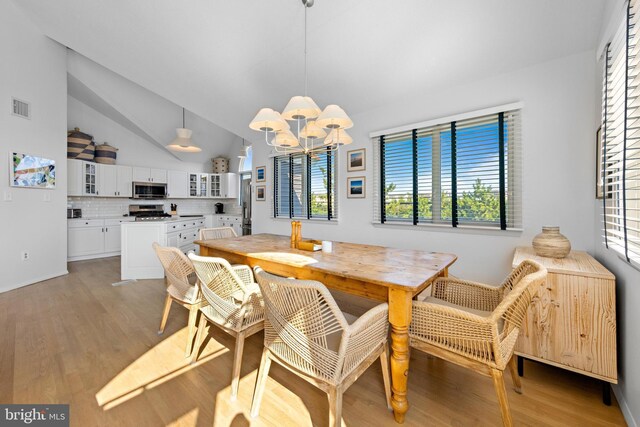 dining space featuring a notable chandelier, light wood-type flooring, and vaulted ceiling