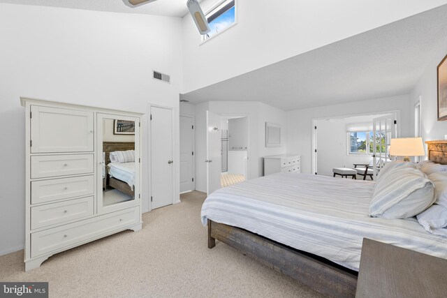 bedroom with a high ceiling, ensuite bath, and light colored carpet