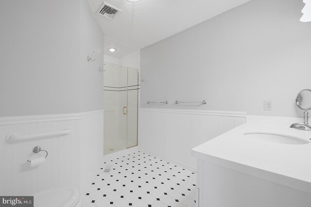 bathroom with a textured ceiling, walk in shower, vanity, and toilet