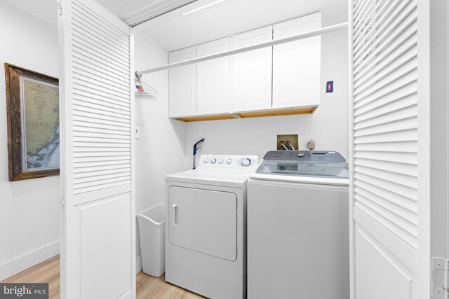 laundry area with light wood-type flooring, washer and dryer, and cabinets