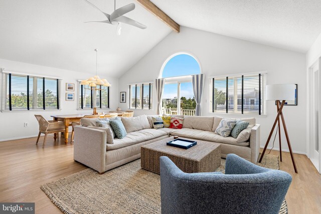 living room featuring ceiling fan with notable chandelier, light hardwood / wood-style floors, and lofted ceiling with beams