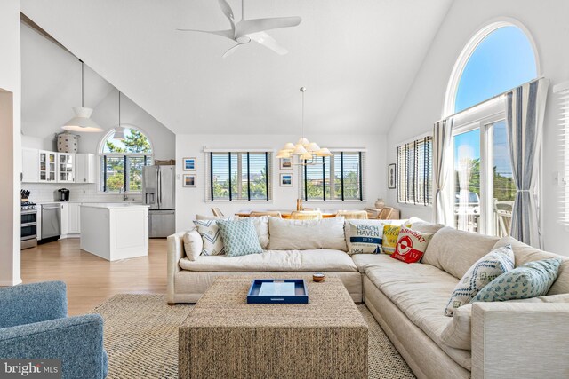 living room with ceiling fan with notable chandelier, light wood-type flooring, high vaulted ceiling, and sink