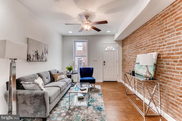 living room with light wood-type flooring, ceiling fan, and brick wall