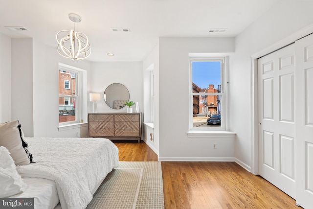 bedroom featuring multiple windows, a chandelier, light hardwood / wood-style floors, and a closet