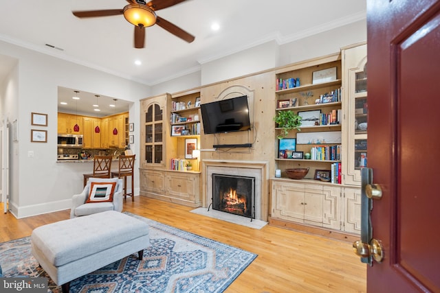 living room featuring a premium fireplace, ceiling fan, ornamental molding, and light wood-type flooring