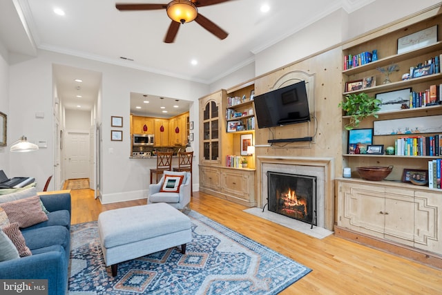 living room with light wood-type flooring, ceiling fan, a fireplace, and ornamental molding