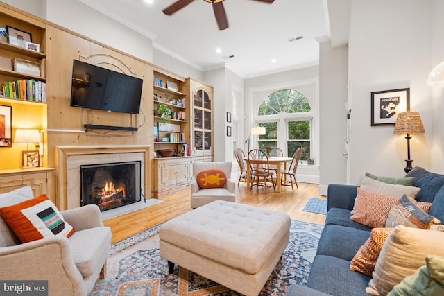 living room featuring crown molding, a premium fireplace, ceiling fan, and light wood-type flooring