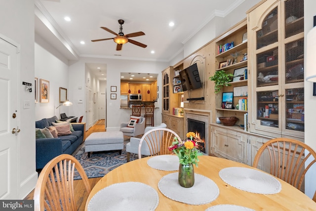 dining space featuring a fireplace, ornamental molding, hardwood / wood-style flooring, and ceiling fan