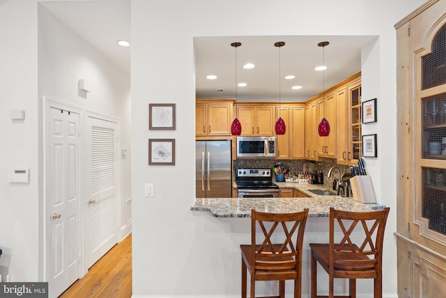 kitchen featuring decorative light fixtures, backsplash, stainless steel appliances, sink, and light wood-type flooring