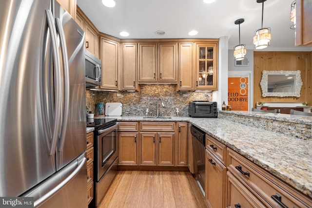 kitchen featuring light stone countertops, stainless steel appliances, sink, decorative backsplash, and light wood-type flooring