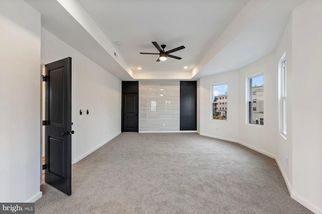 carpeted spare room with ceiling fan and a tray ceiling