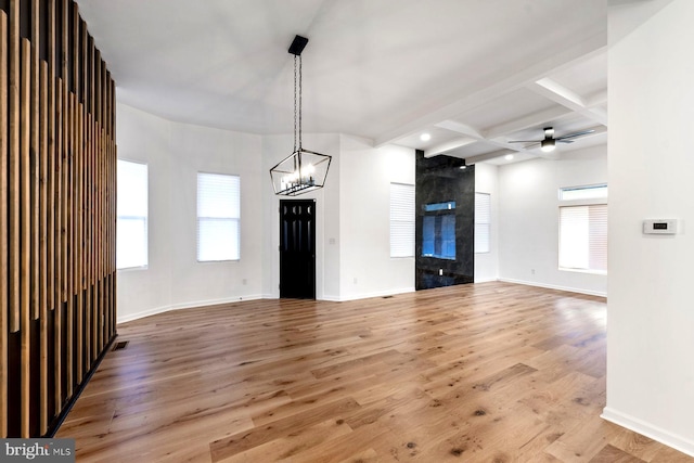 unfurnished living room with beamed ceiling, ceiling fan with notable chandelier, wood-type flooring, and coffered ceiling