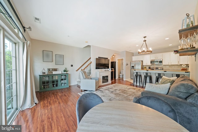 living room featuring baseboards, visible vents, a glass covered fireplace, wood finished floors, and a chandelier