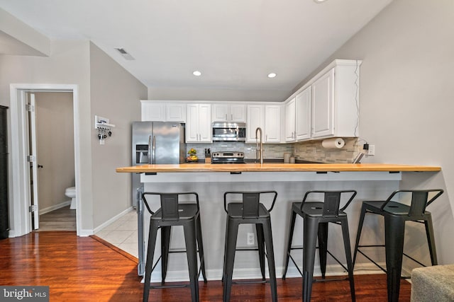 kitchen with a peninsula, visible vents, wooden counters, appliances with stainless steel finishes, and tasteful backsplash