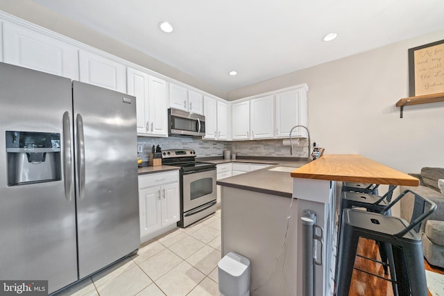 kitchen featuring appliances with stainless steel finishes, white cabinetry, a sink, a peninsula, and a kitchen bar