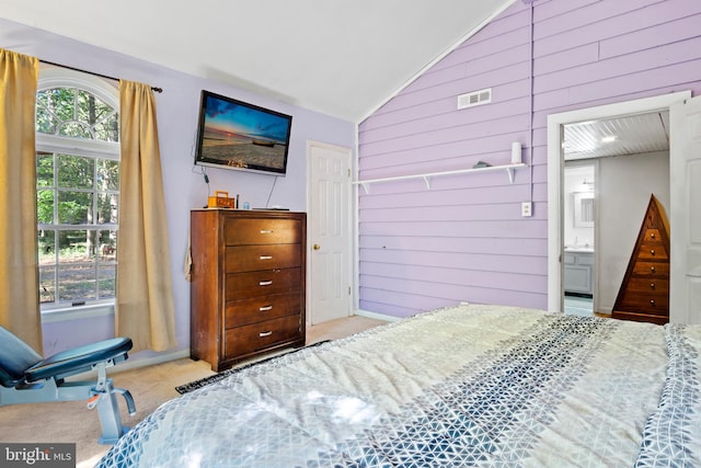 carpeted bedroom with lofted ceiling, wooden walls, and ensuite bathroom