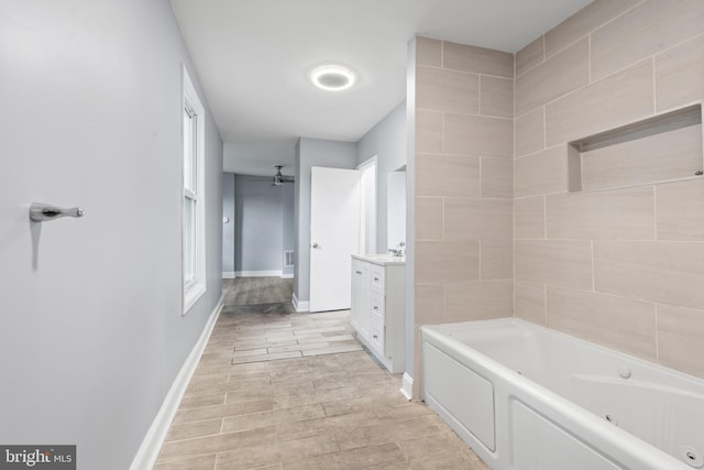 bathroom with wood finish floors, a ceiling fan, vanity, baseboards, and a tub with jets