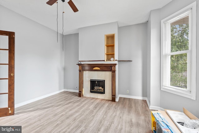 unfurnished living room with a tile fireplace, ceiling fan, baseboards, and wood finished floors