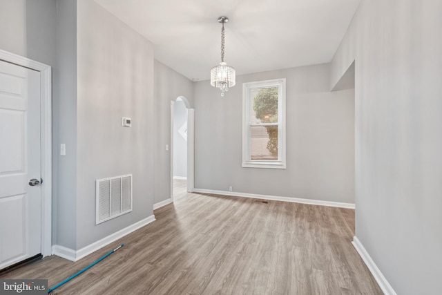 unfurnished dining area with arched walkways, visible vents, baseboards, and wood finished floors