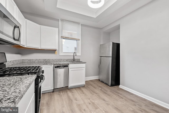 kitchen featuring baseboards, white cabinets, a raised ceiling, appliances with stainless steel finishes, and a sink