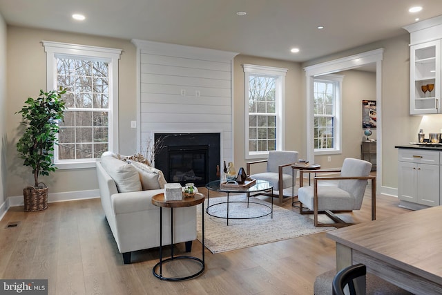 living room with a premium fireplace, visible vents, baseboards, light wood-style floors, and recessed lighting