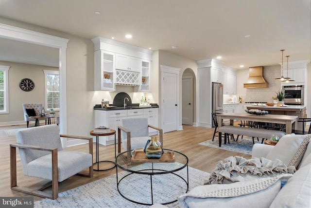 living area with arched walkways, light wood-type flooring, baseboards, and recessed lighting