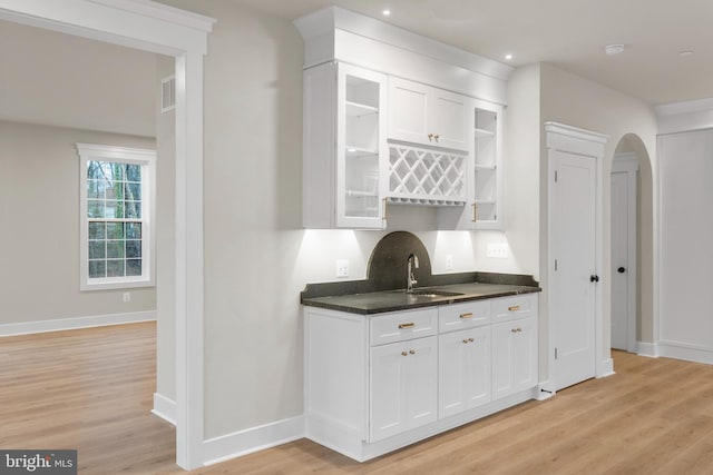 bar with light wood finished floors, baseboards, arched walkways, and a sink