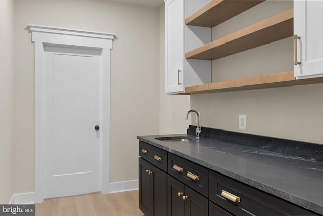 bar with light wood finished floors, a sink, and baseboards