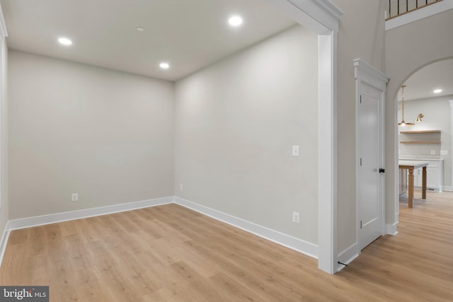 unfurnished room with baseboards, recessed lighting, arched walkways, and light wood-style floors