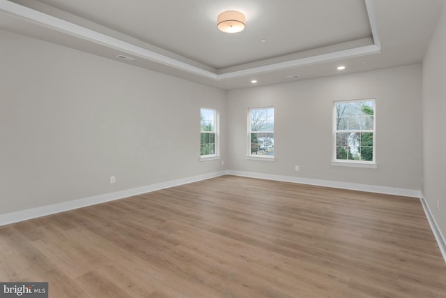 spare room featuring light wood-style floors, baseboards, and a raised ceiling