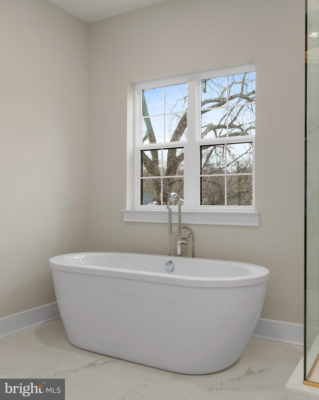 full bathroom with marble finish floor, a freestanding tub, and baseboards