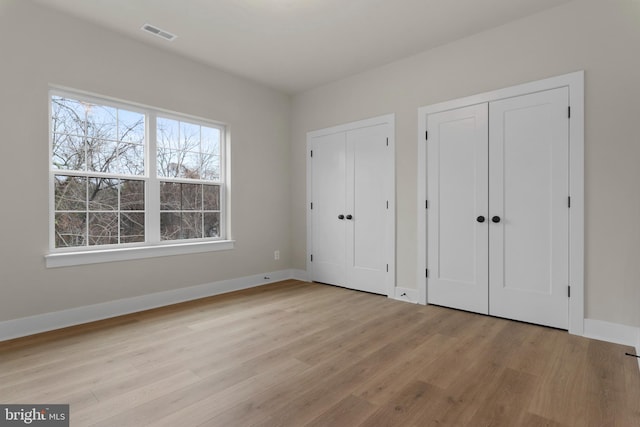 unfurnished bedroom featuring multiple closets and light wood-type flooring