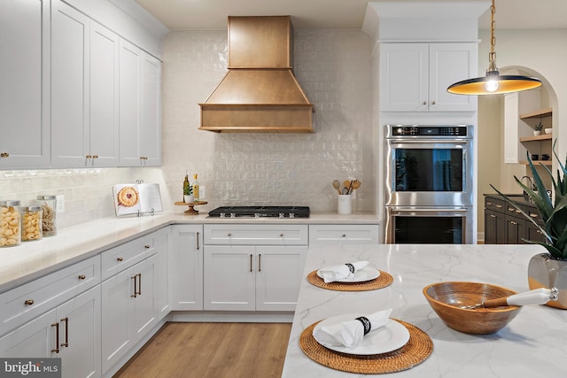 kitchen with light wood-style flooring, premium range hood, double oven, gas stovetop, and backsplash