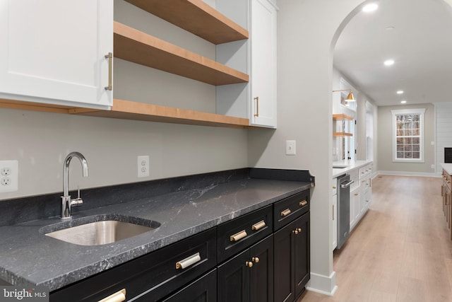 kitchen featuring light wood-style floors, dark cabinets, white cabinets, and a sink