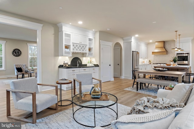 living area featuring arched walkways, light wood-style floors, baseboards, and recessed lighting