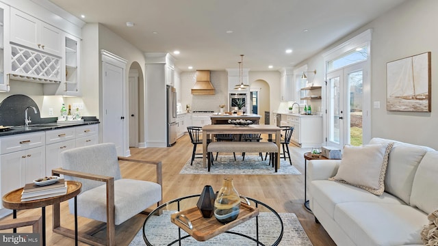 living room with arched walkways, light wood-type flooring, indoor wet bar, and recessed lighting