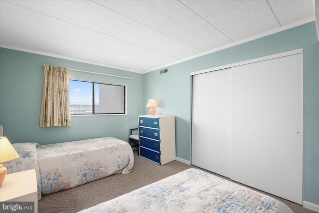 carpeted bedroom with baseboards, crown molding, visible vents, and a closet