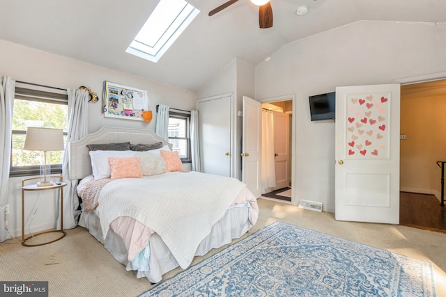 bedroom featuring multiple windows, vaulted ceiling with skylight, light carpet, and ceiling fan