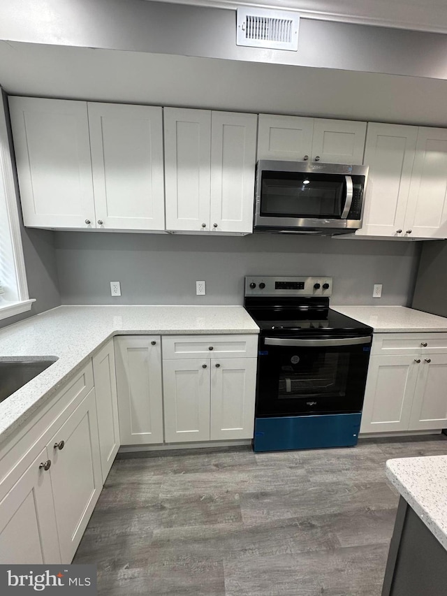 kitchen with light stone countertops, hardwood / wood-style flooring, stainless steel appliances, and white cabinets