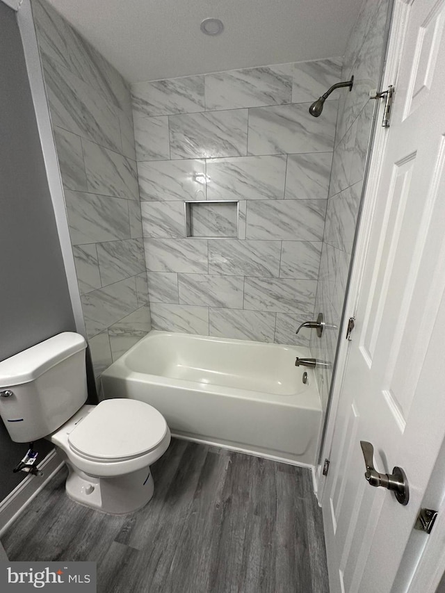 bathroom featuring tiled shower / bath combo, toilet, hardwood / wood-style flooring, and a textured ceiling